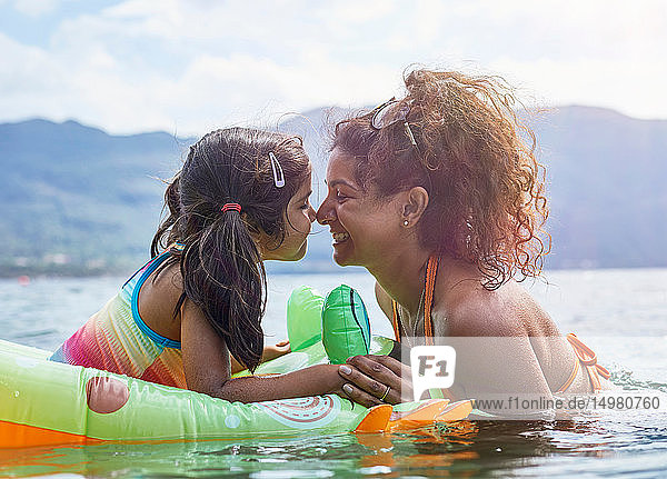 Mutter reibt mit Tochter Nasen an aufblasbaren Fröschen im See