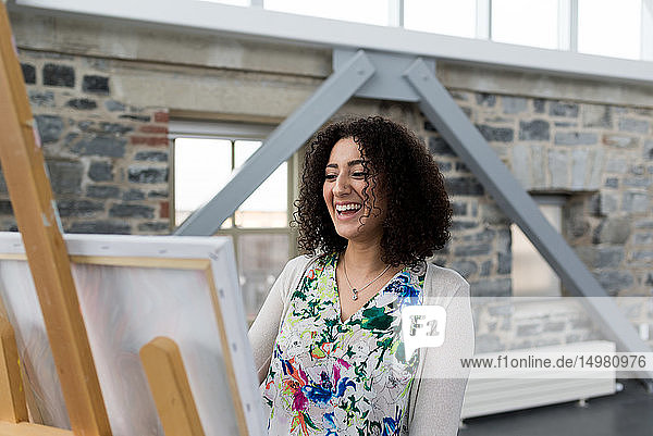 Junge Malerin lacht  während sie im Atelier Leinwand malt