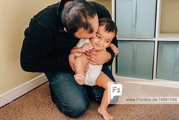 Father kneeling on nursery floor playing with baby son