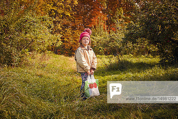 Girl with bag of fresh picked apples in orchard