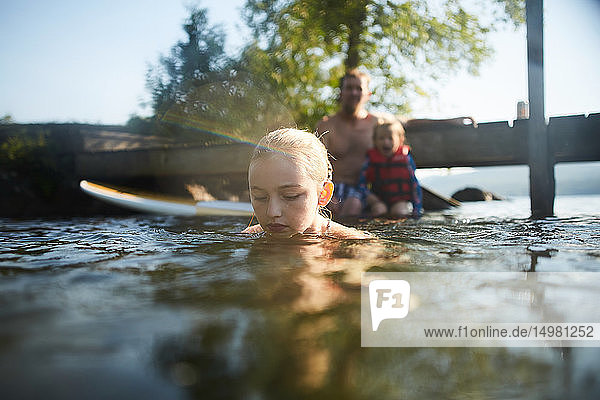 Mädchen schwimmt und spielt im See  Vater und Schwester im Hintergrund