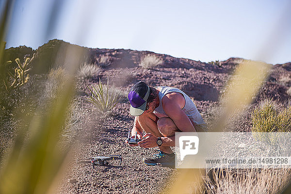 Man squatting in desert looking at control panel for drone (unmanned aerial vehicle)
