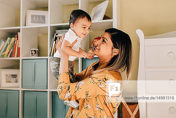 Mother holding up baby son in nursery