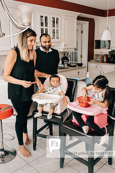 Paar mittlerer Erwachsener in der Küche mit Tochter und kleinem Sohn auf Hochstühlen