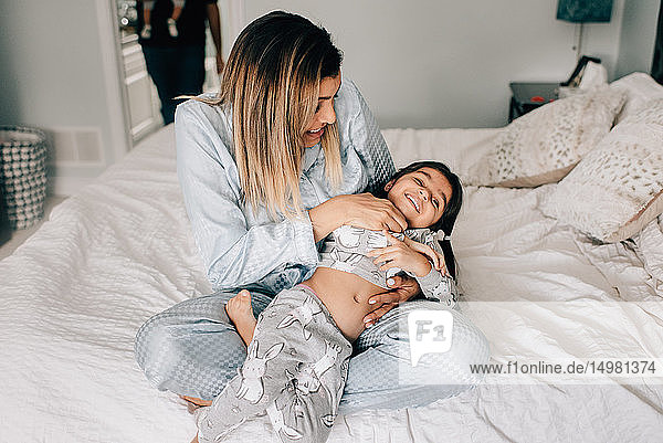 Girl being tickled by her mother on bed in morning