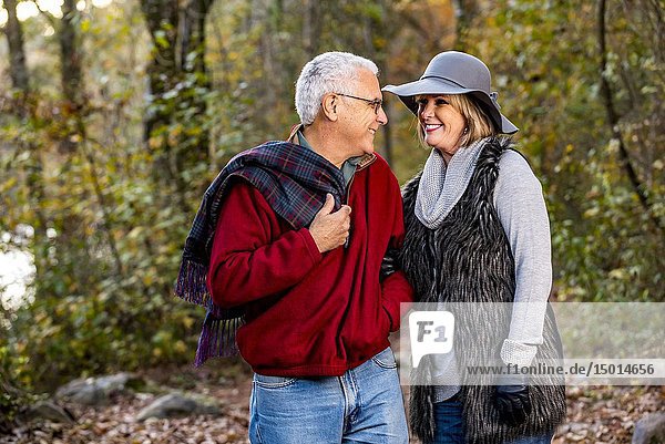 A happy 65 year old man and a 59 year old blond woman hugging and smiling at each other in a forest setting.