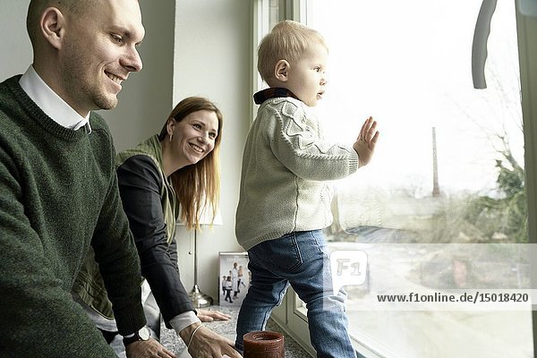 Parents with baby toddler child at window  looking outside  in Cottbus  Brandenburg  Germany.