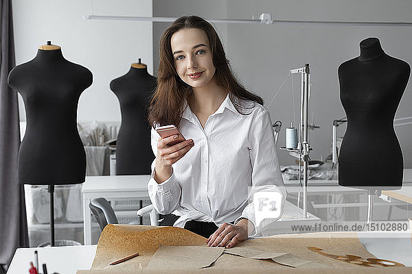 Modedesigner mit Smartphone im Atelier