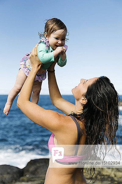 Mutter hält ihr kleines Mädchen über dem Meer