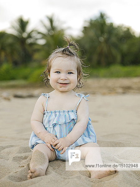 Kleines Mädchen im blauen Kleid am Strand sitzend
