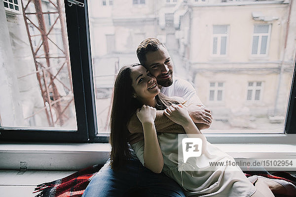 Junges Paar umarmt sich am Wohnungsfenster