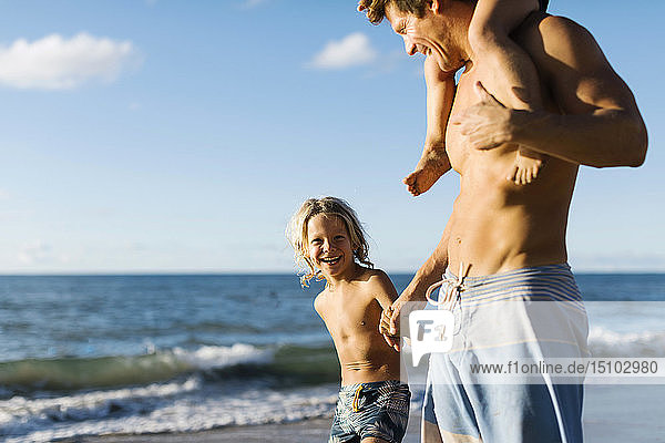 Mann geht mit seinen Kindern am Strand spazieren