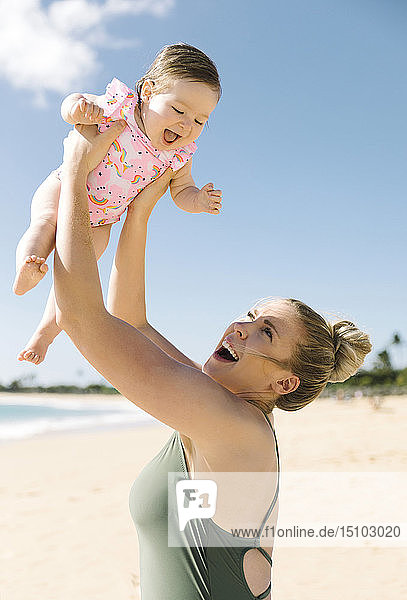 Mutter hält ihr kleines Mädchen am Strand in der Luft