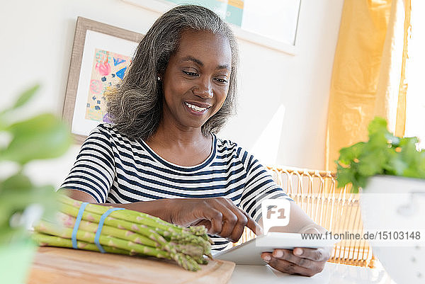 Lächelnde reife Frau schaut auf ein digitales Tablet