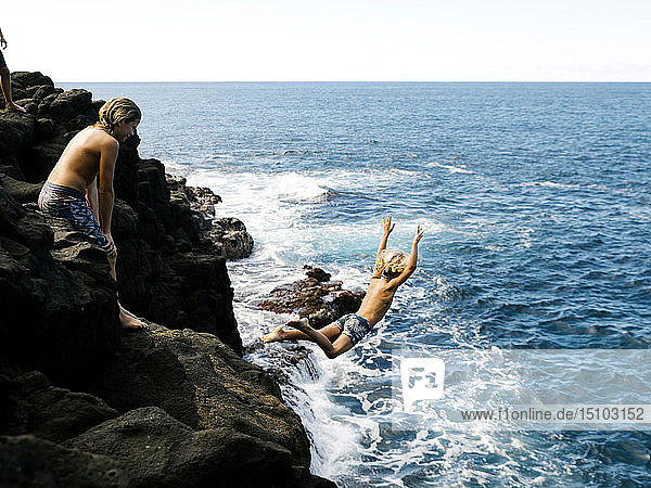 Boy jumping off cliff by sea
