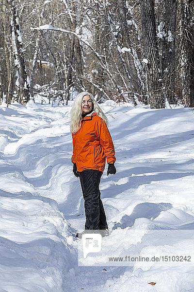 Ältere Frau in orangefarbenem Mantel bei kahlen Bäumen im Schnee