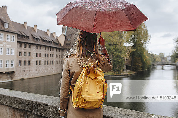 Woman wearing backpack holding umbrella by river in Nuremberg  Germany