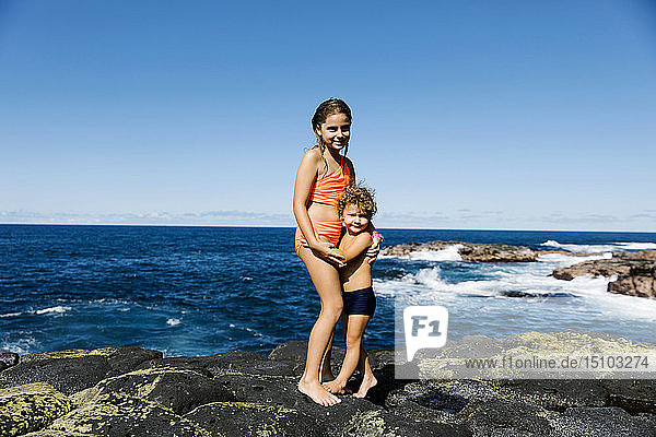 Bruder und Schwester umarmen sich auf einem Felsen am Meer