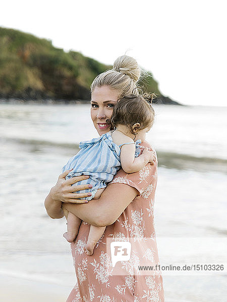 Frau hält ihre kleine Tochter am Strand