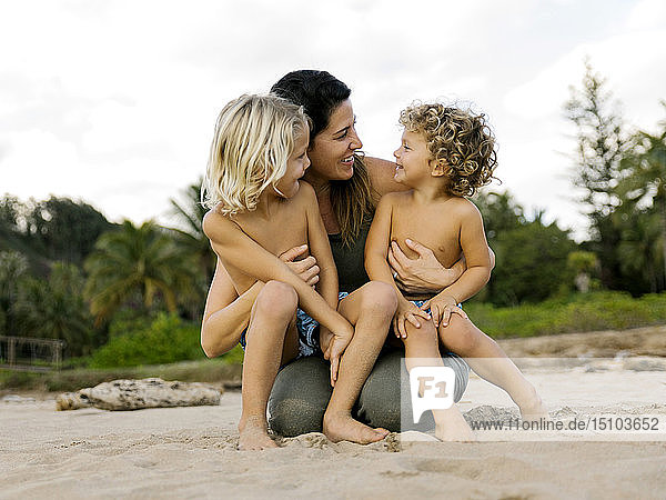 Woman with her sons sitting on her lap on beach