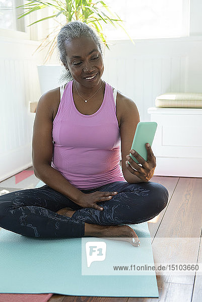 Reife Frau mit Smartphone auf Yogamatte sitzend