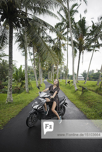 Young woman on motorcycle by palm trees in Bali  Indonesia