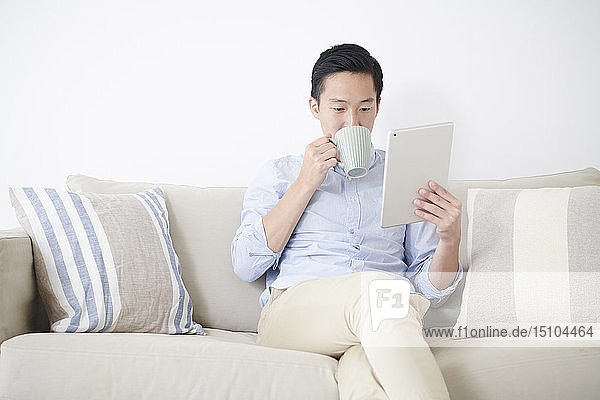 Young Japanese man using tablet on the sofa