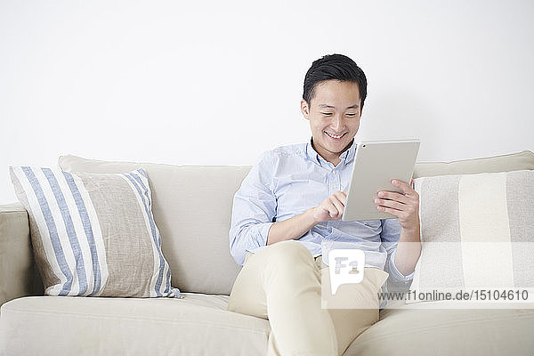 Junger japanischer Mann mit Tablet auf dem Sofa
