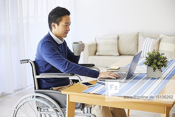Japanischer junger Mann im Rollstuhl arbeitet von zu Hause aus