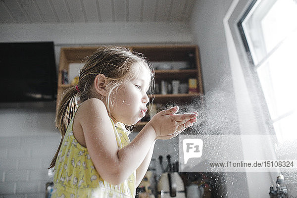 Kleines Mädchen bläst in der Küche Mehl in die Luft