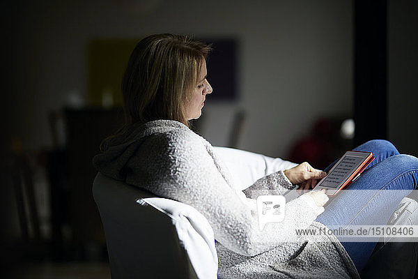 Frau sitzt im Sessel und liest E-Book