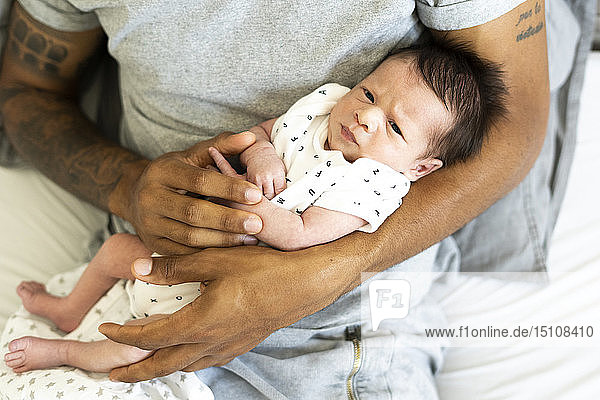 Porträt eines Neugeborenen in den Armen des Vaters im Bett