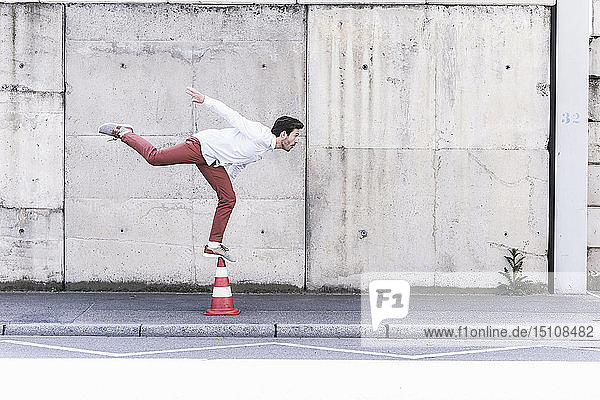 Junger Mann balanciert auf Verkehrskegel vor Betonmauer