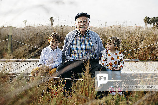 Porträt eines Großvaters  der mit seinen Enkelkindern Seite an Seite an der Strandpromenade sitzt
