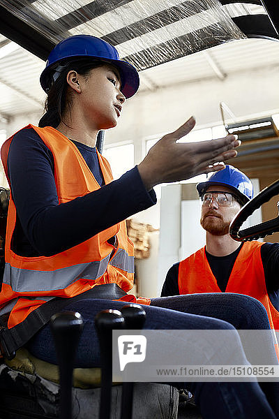 Mann spricht mit einer Arbeitnehmerin auf einem Gabelstapler in einer Fabrik