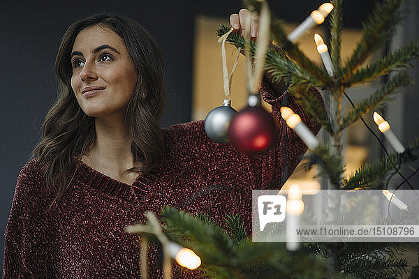 Junge Frau schmückt Weihnachtsbaum und schaut weg