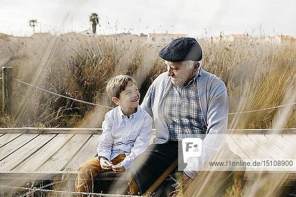 Großvater sitzt mit seinem Enkel an der Strandpromenade und unterhält sich
