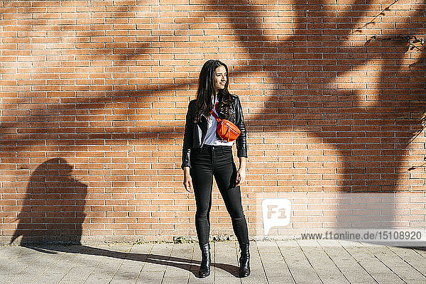 Young woman with a red bag waiting at a brick wall in the background and a shadow of tree