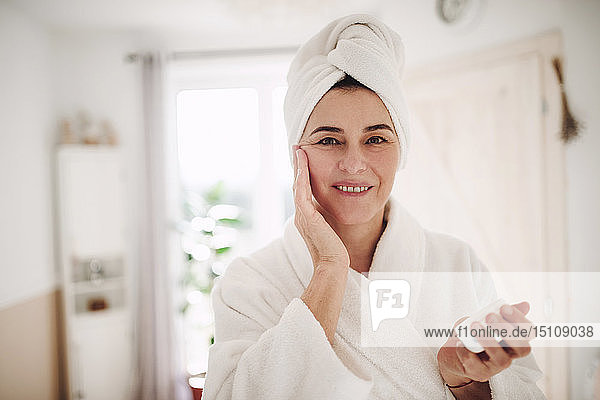 Porträt einer reifen Frau in einem Badezimmer zu Hause  die Feuchtigkeitscreme aufträgt