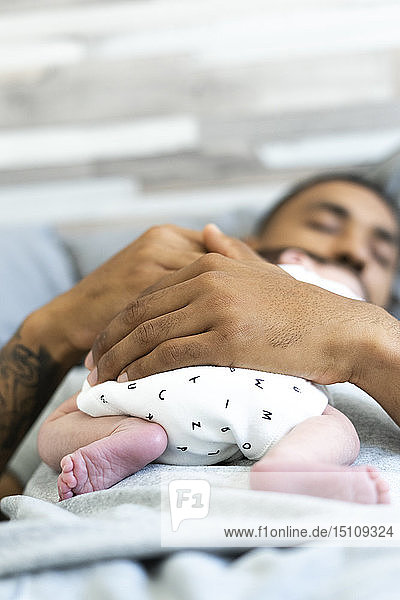 Mann schläft im Bett und hält sein Neugeborenes