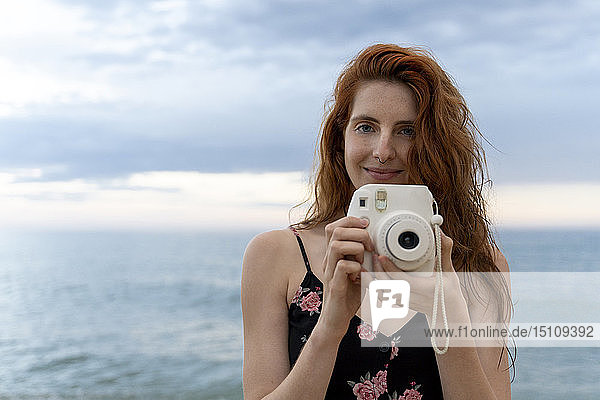 Portrait of redheaded young woman with nose piercing taking pictures with camera