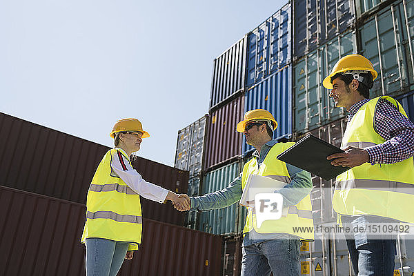 Arbeiter schütteln Hände vor Frachtcontainern auf einem Industriegelände