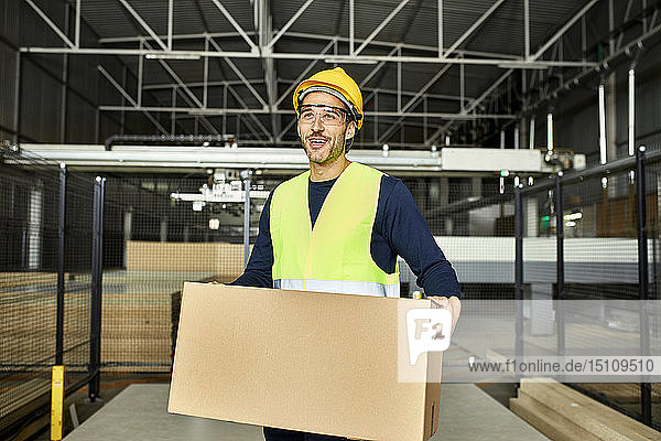 Porträt eines lächelnden Arbeiters  der eine Kiste in einem Fabriklager trägt