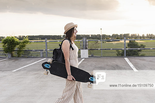 Young woman with longboard walking on parking deck