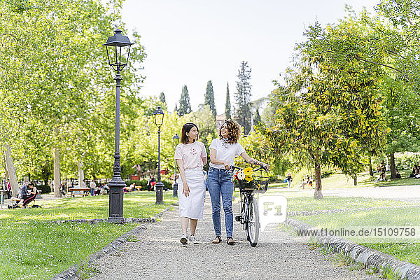 Two women with bicycle walking in park