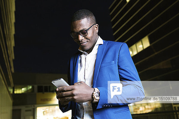 Junger Geschäftsmann in blauer Anzugjacke und mit Smartphone in der Nacht