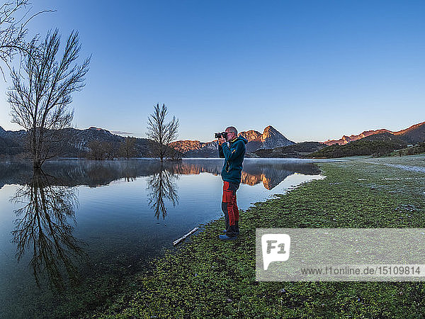Spain  Asturias  Camposolillo  Cantabrian Mountains  senior man taking a photo at the seashore of Porma reservoir