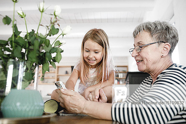 Glückliche Großmutter mit Handy und Enkelin zu Hause