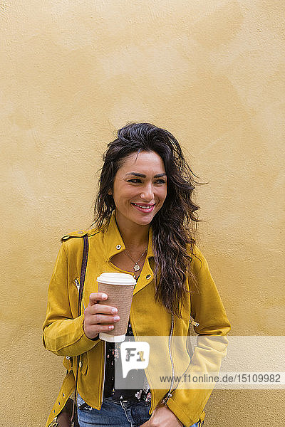 Porträt einer jungen Frau in gelber Lederjacke  die eine Tasse Kaffee hält