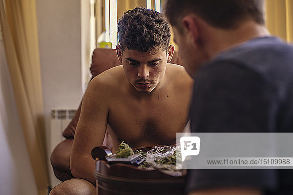 Zwei junge Männer im Wohnzimmer mit Blick auf Marihuana-Knospen